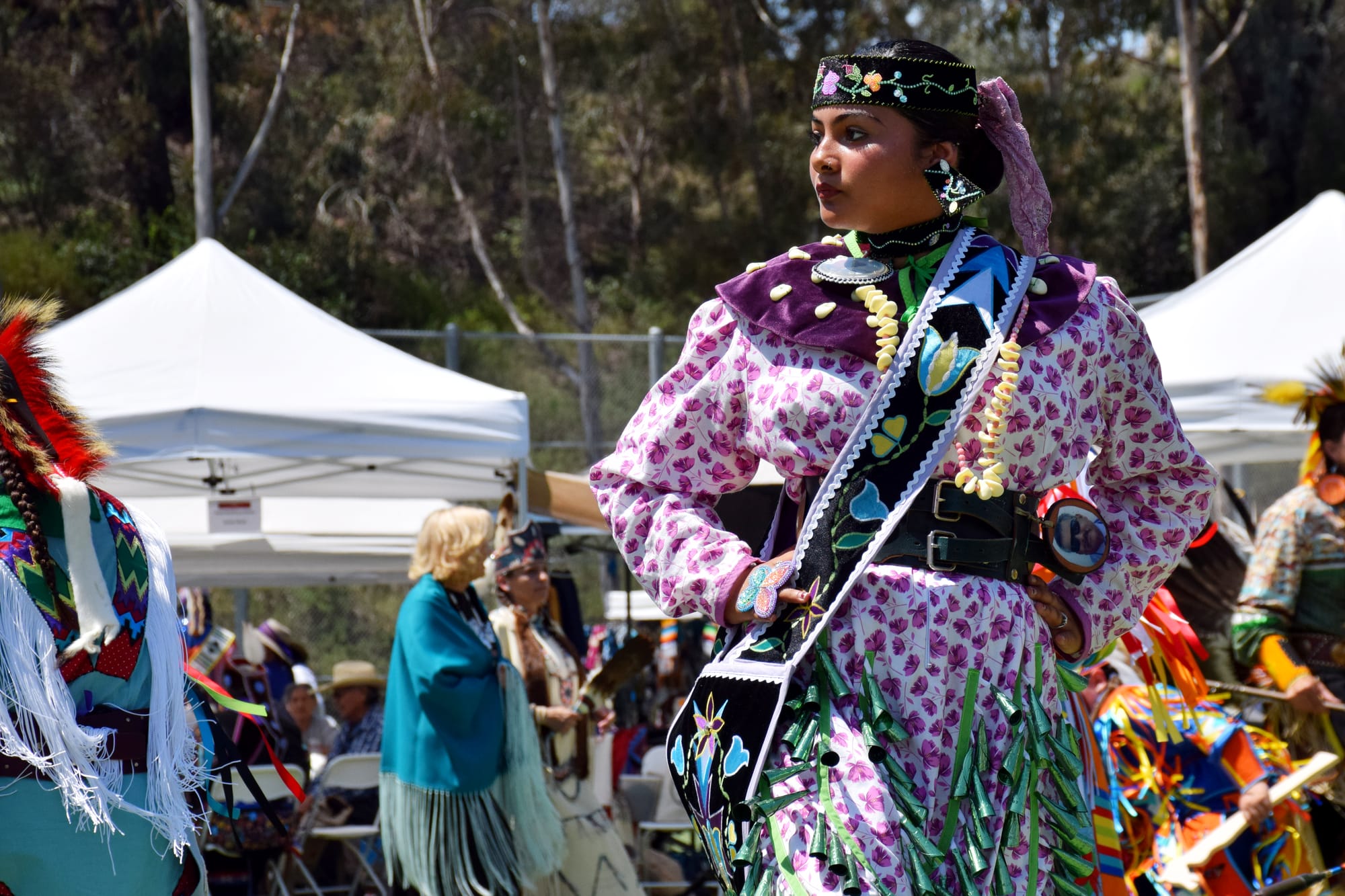 A girl in a jingle dress dances at a powwow, surrounded by other dancers.